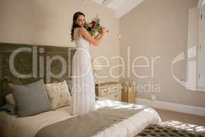 Portrait of beautiful bride holding bouquet while standing on bed