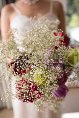 Midsection of bride holding bouquet at home