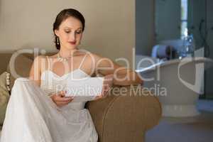 Beautiful bride reading wedding card while sitting on sofa