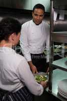 Chef handing food dish to waitress at order station