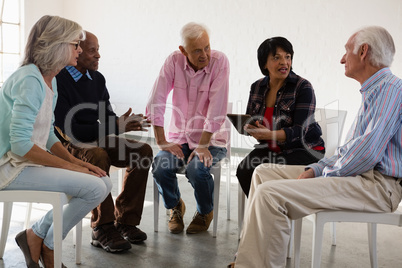 Senior friends discussing over tablet computer while sitting on chair