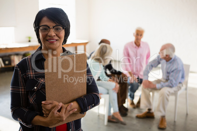 Portrait of senior female holding clipboard with friends sitting in background