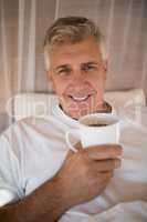 Portrait of happy man having coffee on bed