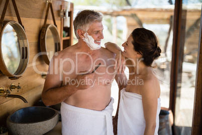 Smiling couple interacting while shaving in cottage