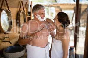 Smiling couple interacting while shaving in cottage