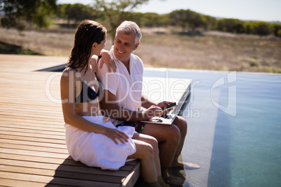 Couple interacting while using laptop near poolside