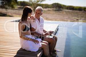 Couple interacting while using laptop near poolside