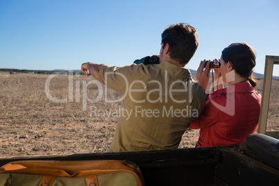 Rear view of couple looking through binoculars at landscape