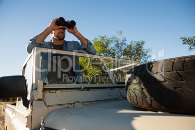 Young man looking through binoculars standing in off road vehicle