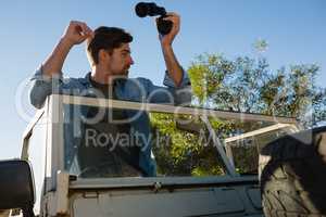 young man holding binoculars looking away while standing in off road vehicle