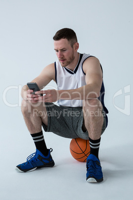 Player sitting on basketball and using mobile phone