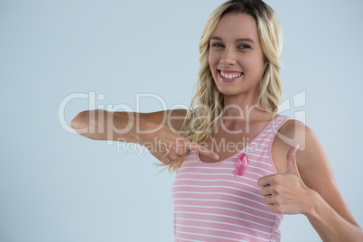 Portrait of smiling woman showing thumbs up while pointing on pink ribbon