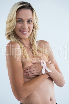 Portrait of smiling woman covering breast with pink ribbon on hand