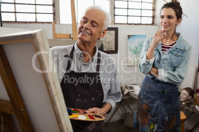 Woman watching while senior man painting on canvas