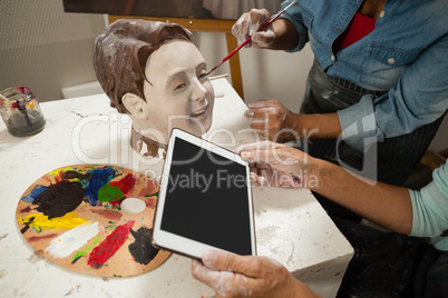 Woman using digital tablet while painting a sculptor