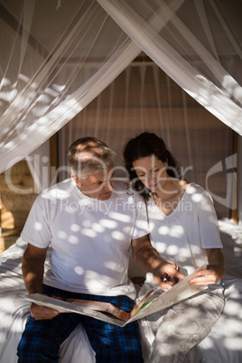 Couple looking at map while relaxing on canopy bed
