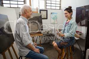 Woman interacting with senior man while sketching on canvas