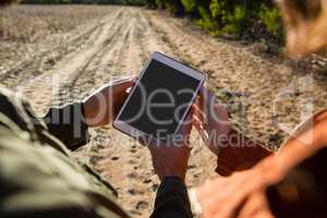 Cropped hands of couple using tablet on field