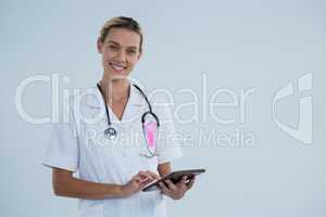 Portrait of female doctor with Breast Cancer Awareness ribbon using tablet computer