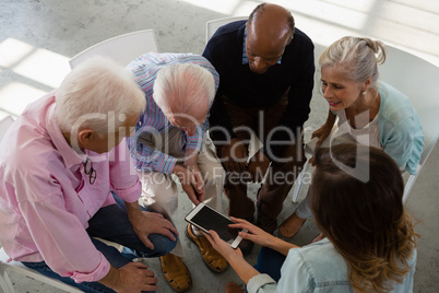 High angle view of teacher showing tablet while sitting with senior adults