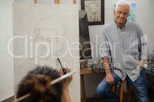 Senior man watching while artist drawing on canvas
