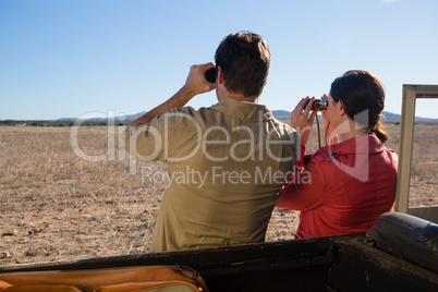 Rear view of couple by off road vehicle looking through binoculars