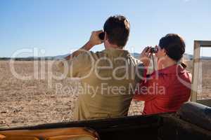 Rear view of couple by off road vehicle looking through binoculars