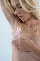 Woman covering breast while looking at pink ribbon
