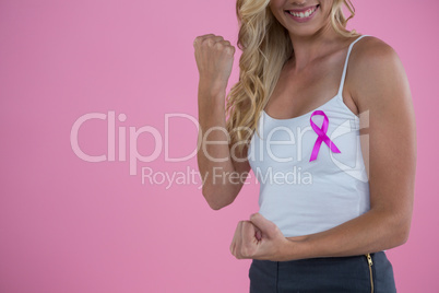 Mid section of smiling woman with Breast Cancer Awareness ribbon clenching fist while
