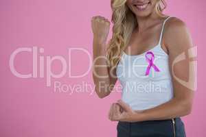 Mid section of smiling woman with Breast Cancer Awareness ribbon clenching fist while