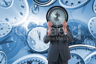 Composite image of businessman holding clock in front of his face