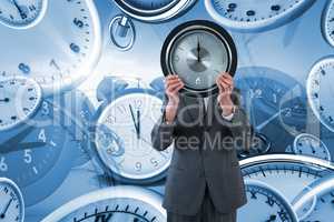 Composite image of businessman holding clock in front of his face