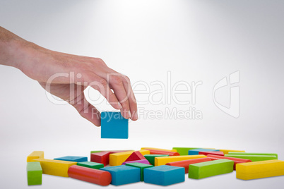 Composite image of cropped hand arranging colorful blocks