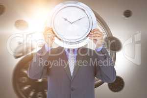 Composite image of businessman holding wall clock in front of face