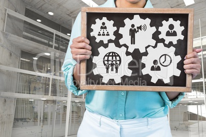 Business woman holding a blackboard with people in cogs graphics against office background