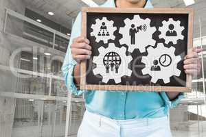 Business woman holding a blackboard with people in cogs graphics against office background