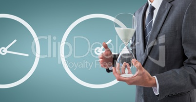 Business man holding a sand clock against background with clocks