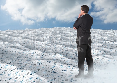 Businessman in sea of documents under sky clouds