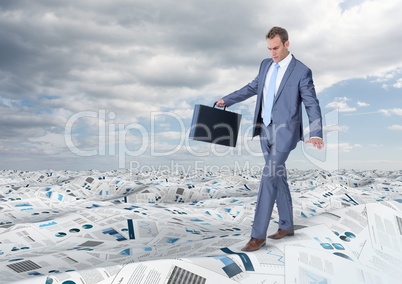 Businessman holding briefcase balancing in sea of documents under sky clouds