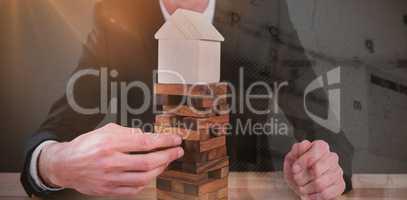Composite image of businessman arranging blocks with model house on top
