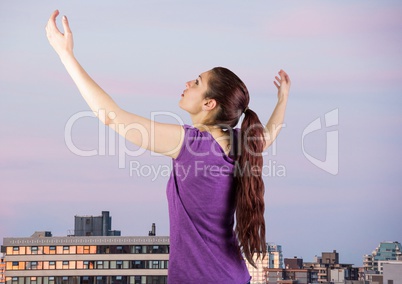 Woman arms in air against buildings and evening sky