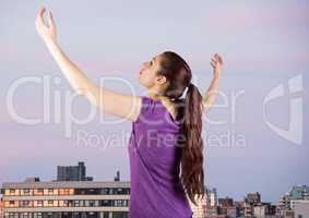 Woman arms in air against buildings and evening sky