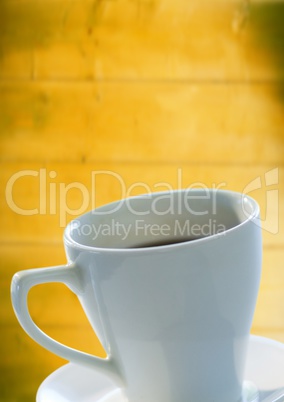White coffee cup and saucer against blurry yellow wood panel