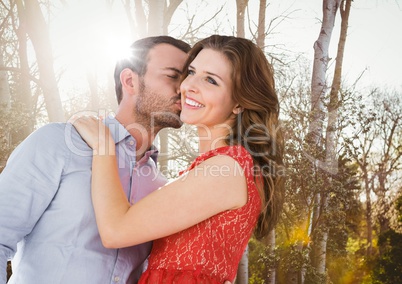 Man kissing woman on cheek against blurry trees with flare