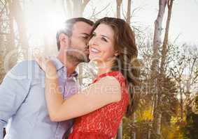 Man kissing woman on cheek against blurry trees with flare
