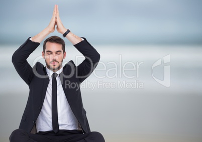 Business man meditating against blurry beach