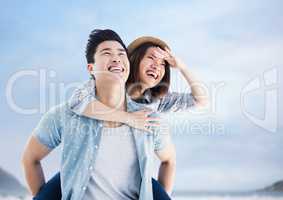 Couple piggy back against sky and blurry beach