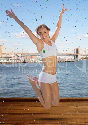 Woman jumping in air against water and skyline and confetti