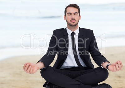 Business man meditating against blurry beach