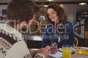 Woman looking at businessman with tablet in cafe